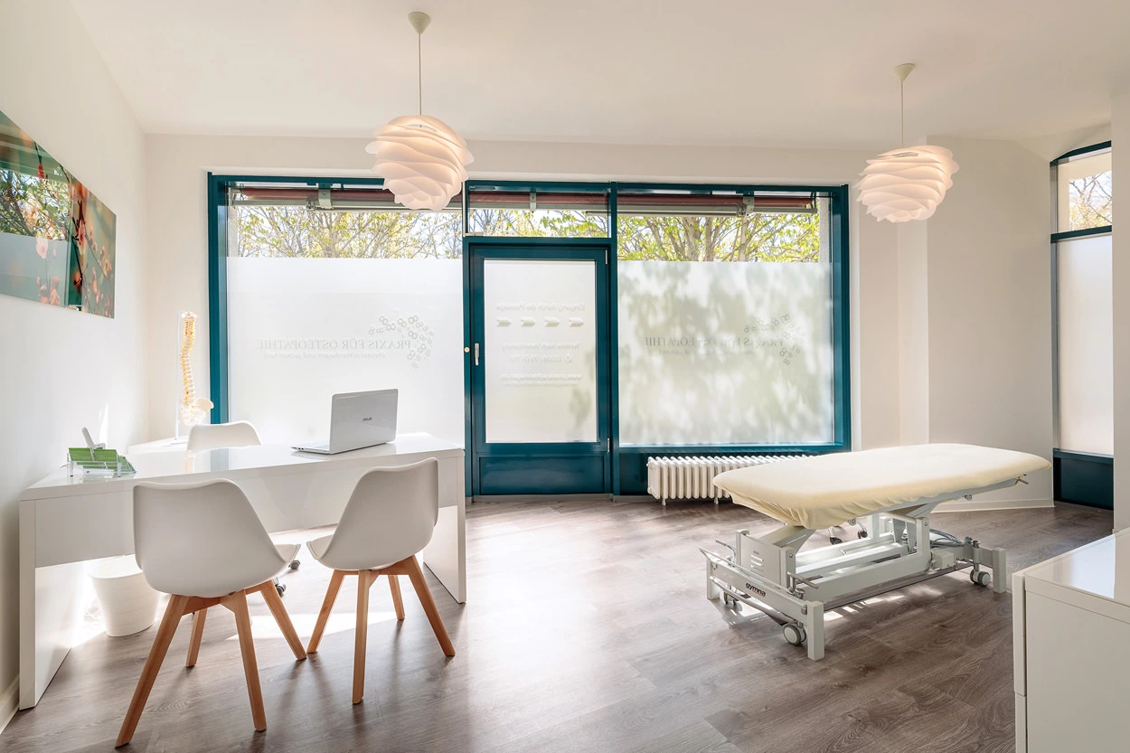 Behandlungsraum der Praxis für Osteopathie in Bernau mit Behandlungsliege, Schreibtisch und Stühlen
